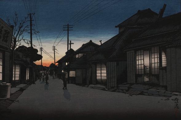 Dusk falls on a little street in Choshi, Chiba. Houses line up on either side of the street, their paper sliding doors and windows lit from within as the night approaches. A small number of pedestrians carrying baskets and other bundles walk along the street; above their heads, utility poles follow the road, drawing straight lines in the air with their wires. Above, a deep blue sky takes over from the remnants of a coral sunset fading at the horizon.