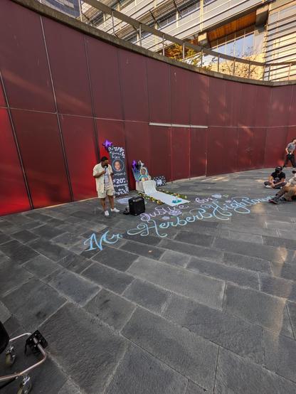 Herbert Hightower Jr's sister Castil begins the vigil holding a mic and stands in front of pictures of Herbert, flowers and a white carpet of candles.

Herbert's name is emblazoned on the ground in flowery chalk art.