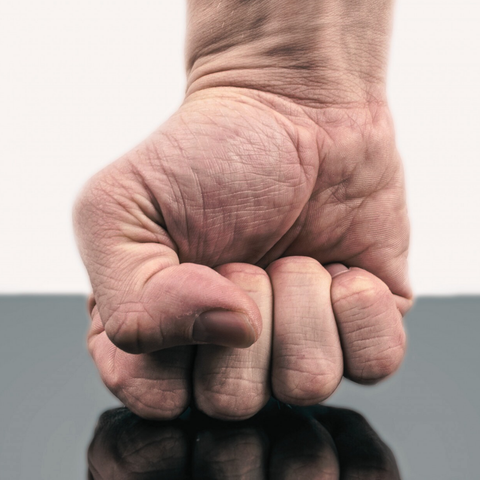 Un puño cerrado golpea la superficie pulida de una mesa.