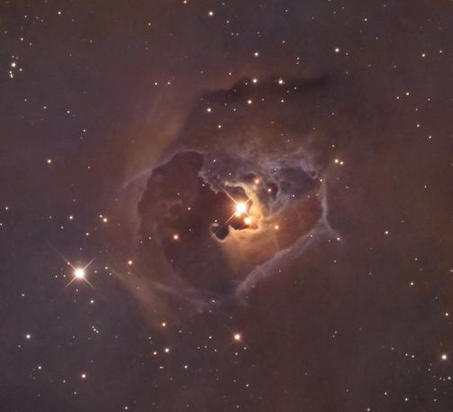 A bright yellow star with two close companions below it, embedded in a roughly pear-shaped bubble of gas. The "pointy end" of the pear is at right. Within the general boundary of the bubble we have a relatively dark region on the left and a filigree of wispy cloudiness on the right.