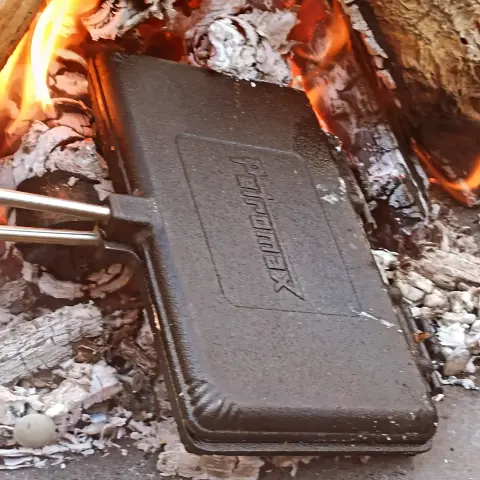 Ein Lagerfeuer, in dem ein gußeisenes Waffeleisen liegt.