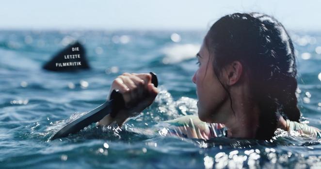 Frau mit Messer erspäht eine Haiflosse neben sich im tiefen Wasser. Szene aus dem Film "Something in the Water" als Cover des Podcasts "Die Letzte Filmkritik".