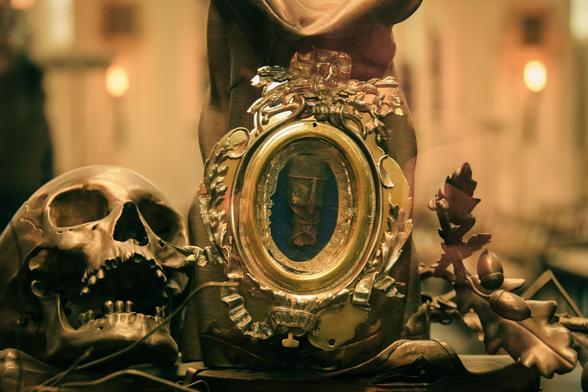 Close-up view of a saint's reliquary, coated in gold. On the left is a skull; in the middle a medallion containing a piece of bone; one the right oak-tree leaves and acorns.