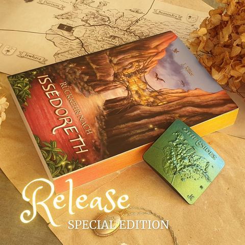 Das Taschenbuch "Rückkehr nach Issedoreth" mir Farbschnitt arrangiert auf Pergamentpapier mit Goodies wie einem Medaillon, darüber der Text: Release Special Edition