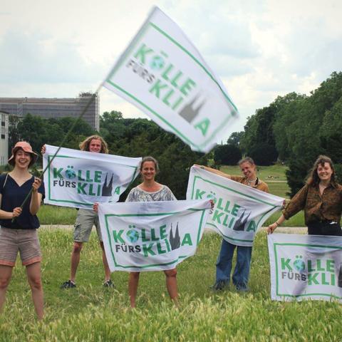 Fünf Menschen präsentieren die Kölle fürs Klima Fahnen auf der Uniwiese in Köln