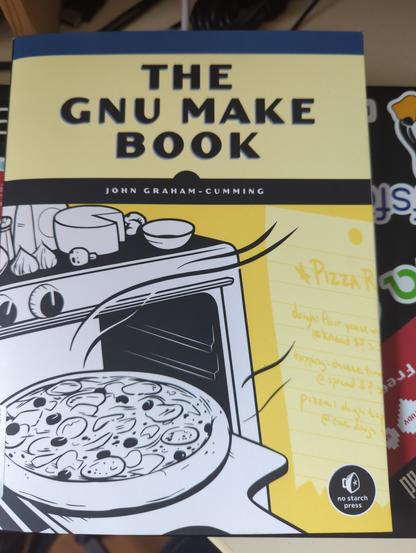 A book lying on a laptop. The book shows a comic oven with a pizza ready for eating.
The book is called 'The GNU make book', by John Graham-Cumming.
