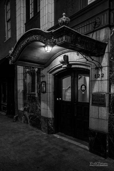 A 1914 Art Deco entrance and facade on an 1849 stone building lit by a single light over the entrance and nearby street lights.