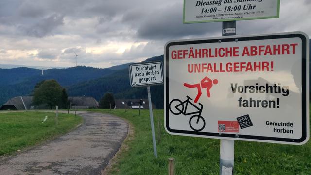 Zwei Schilder hintereinander. Eines gibt die Info "Gefährliche Abfahrt Unfallgefahr! Vorsichtig fahren!" mit Radli Piktogramm. Das andere trägt den Text "Durchfahrt nach Horben gesperrt"