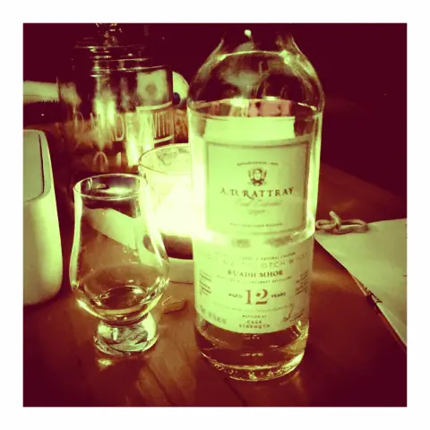 Eine Flasche Whisky mit einem Glas auf einem Tisch, im Hintergrund steht ein brennendes Windlicht.