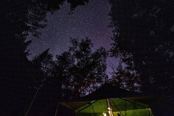 The night sky, full of stars, over a popup camper lit from inside.
