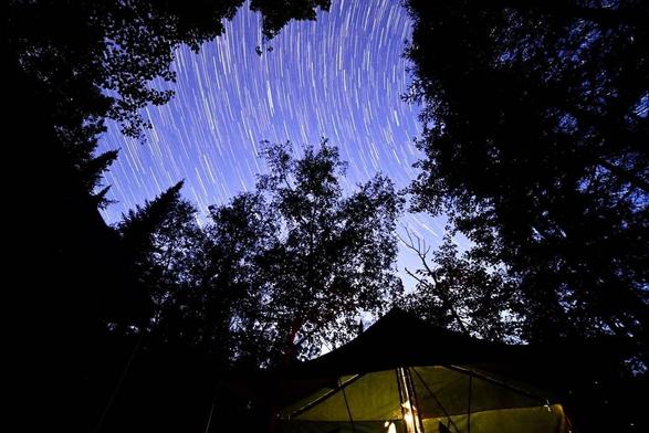 Star trails over a camper lit from inside.
