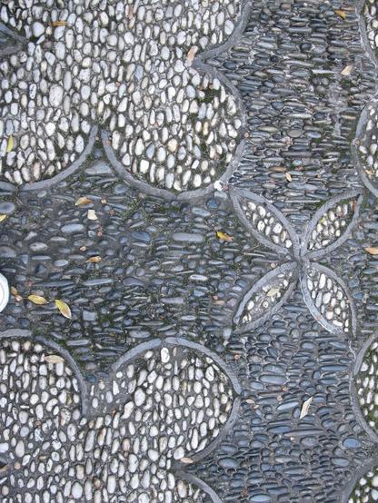 Paving made from small rounded stones set close together. Dark grey stones form the background. Lighter grey pebbles are set in flower patterns.