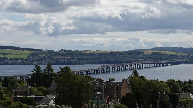 Looking down from the Western Cemetery towards the River Tay with the Tay Railway Bridge running diagonally up/right across the water. Green wooded hills of Fife are behind.