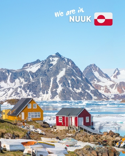 A picturesque scene in Nuuk, Greenland, showing colorful houses by the water's edge with snow-capped mountains in the background. The foreground features a few boats on the rocky shore, and floating ice is visible in the water. The text 'We are in Nuuk' is displayed at the top along with the flag of Greenland.