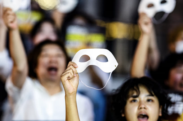 Women in a deepfake pornography protest hold up white masks.