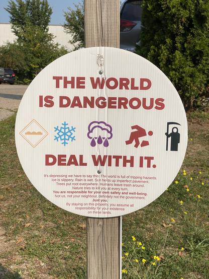 A circular warning sign that reads, "THE WORLD IS DANGEROUS, DEAL WITH IT." Below are icons representing various hazards such as ice, rain, and the grim reaper. The text says, "it's depressing we have to say this. The world is full of tripping hazards. Ice is slippery. Rain is wet. Sun heats up imperfect pavement. Trees put roots everywhere. Humans leave trash around. Nature tries to kill you qt every turn. You are responsible for your own safety and well-being. Not us, not your neighbour, definitely not the government. Just you. By staying on this property, you assume all responsibility for your existence on these lands."