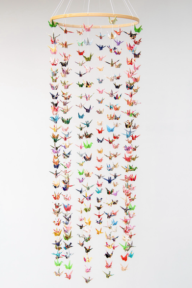 Suspension décorative composée d’une multitude de petites grues multicolores en origami sur un support circulaire en bois