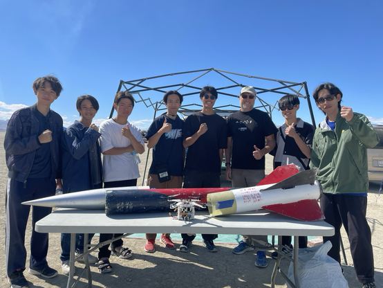 Eight people standing behind a large rocket and a drone payload