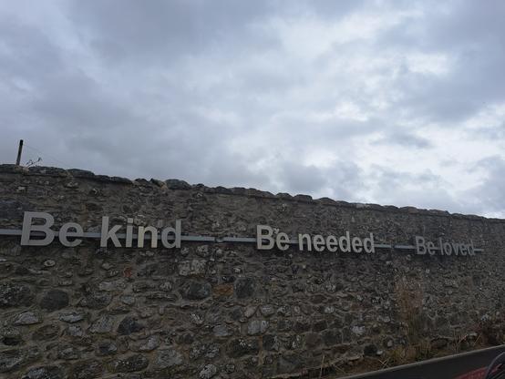 Stone wall with  the message. Be kind.  Be needed. Be loved in 30cm high brushed aluminium lettering.