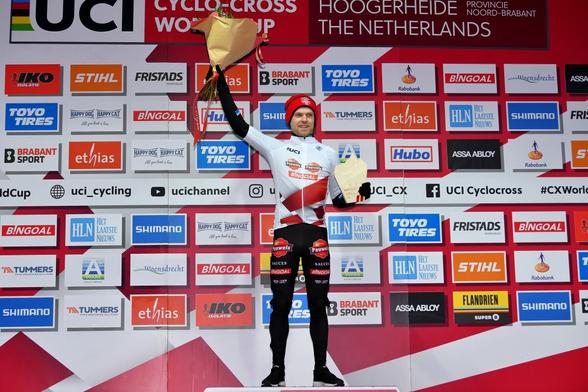 Eli Iserbyt, winner of the Elite Men’s UCI Cyclo-Cross World Cup in 2023-24. Pictured on the podium holding a trophy and bunch of flowers.