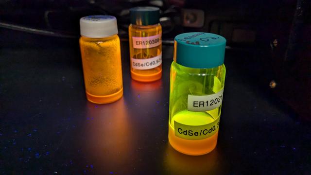 3 vials of quantum dots glowing under a uv light.