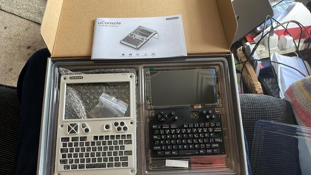 The open box of the uconsole, on the top is the case case in silver metal beside the screen, keyboard and various other components.