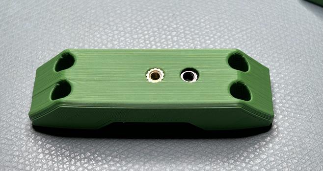 A green printed piece of ASA with two heat set inserts. The left one is brass and is set to a good depth.  The right one is black nickel plated and is about a millimeter too low.  The side of the piece is warped about a millimeter -- the piece is about 50-60 millimeters long and 15 wide.