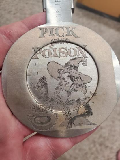 ForLife teapot lid with a poorly laser engraved image. Text on the top reads "Pick your Poison" with a witch working a cauldron.