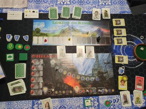 The board game Lord of the Rings is laid out on a table. The top board shows Frodo (currently the Ringbearer) part-way corrupted while Sam remains mostly pure; the Sauron figurine is creeping toward the Hobbits.

The lower board shows the beginning of progress through the Helm's Deep scenario. A dice tray shows the Corruption die has just rolled a damaging 3 Corruption.

The play of Arwen card has allowed the Friendship track to progress a little, gaining Theoden for the Fellowship.