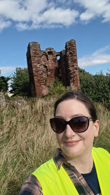A person in a high vis vest in front of the ruin of a castle tower