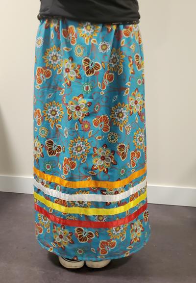 Floral designs on aqua blue fabric with orange, white, yellow & red ribbon bands on bottom. Finished ribbon skirt.