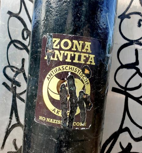 Zona Antifa 
Anti-fascist sticker on black metal pole. It's been scratched at but still visible & removal didn't work