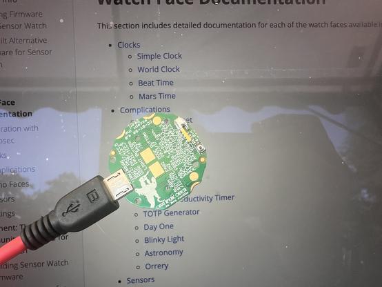 Im Vordergrund sieht nach das "grüne" Board der Sensorwatch, das mit einem USB-Kabel verbunden ist, kurz bevor die neue Firmware installiert wird.
