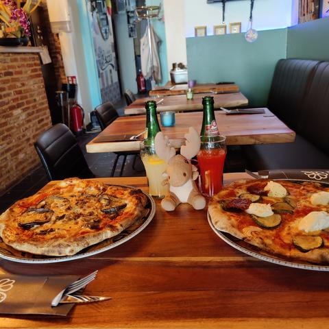 Mr Moose sitting on a wooden table, with two sodas behind him, and pizzas to his sides.

In the left aubergine and scamorza, on the right courgette and burrata