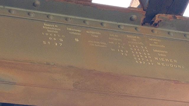 Schlecht lesbare Beschriftung der ausgebauten Fachwerkbrücke.

1. Spalte:

Bauwerk-Nr. 10485 0
Brückenklasse 08 S
Baustahl ST 37

2. Spalte:

Entrostungsverfahren S

3. Spalte:

Ausführende Firma:
<unleserlich> Pflug GmbH
7935 Rei<unleserlich>acker

4. Spalte:

Zeit der Ausführung
von 20.7.75
bis 19.9.75

5. Spalte:

Baustoff-Nr. der
<unleserlich>stoffe

634 55
634 75
635 58
636 90
637 42
637 37

6. Spalte:

<unleserlich> der
Anstrichstoffe (?)

Gehol<unleserlich>werke
Graben

WIEMER
NEUDORF