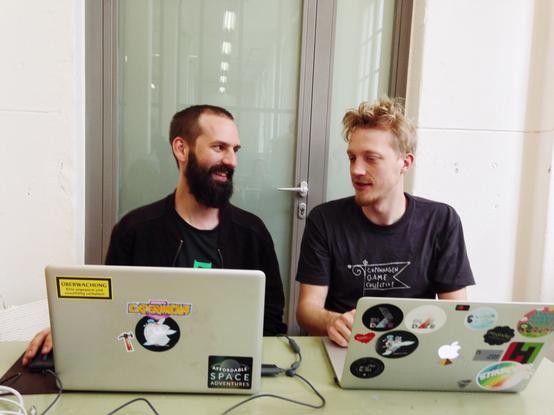 Two people behind laptops. The laptops have stickers on them.