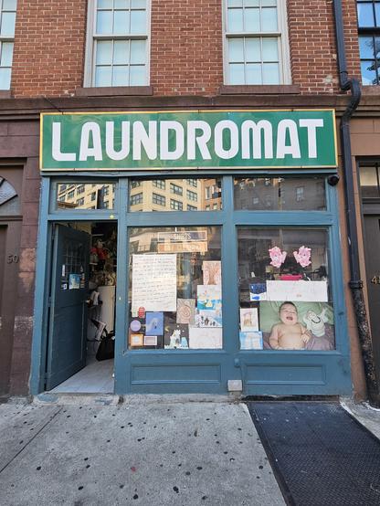 Photograph of a storefront in Greenwich village. A green store sign says "Laundromat" in whote ALLCAPS