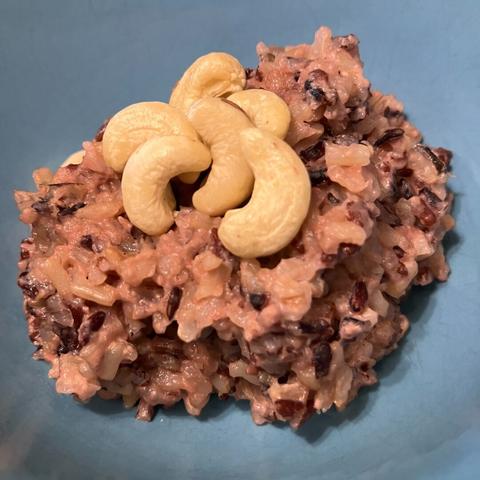 A red rice pudding topped with cashews