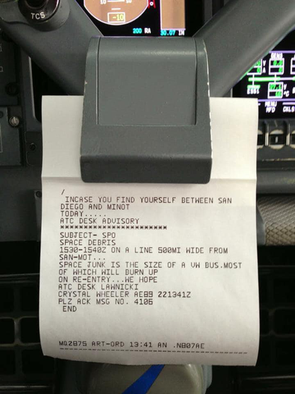 Photograph shows a printed memo clipped to the dash of an aircraft flight deck. The memo reads “In case you find yourself between San Diego and Minot today. ATC Desk Advisory Subject: SPACE DEBRIS. 15:30-15:40 UTC on a line 500 miles wide. Space junk is the size of a Volkswagen bus. Most of which will burn up on re-entry… we hope.”