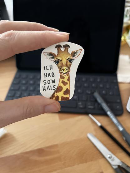 Ich halte eine kleine Aquarellzeichnung in meinen Fingern: der Kopf und der Hals einer Giraffe, die ihre Stirn runzelt. Daneben steht „ich hab so‘n Hals“