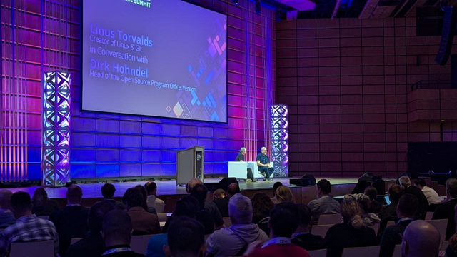 Picture taken from the audience, showing lot of people looking at the stage, with Linus Torvalds (left) and Dirk Hohndel (right).
The atmosphere is sparkling and there are purple lights everywhere.