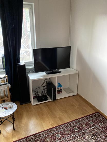 White TV-stand / cabinet with a widescreen TV on top that contains PC, router, Blu-ray player and computer books.