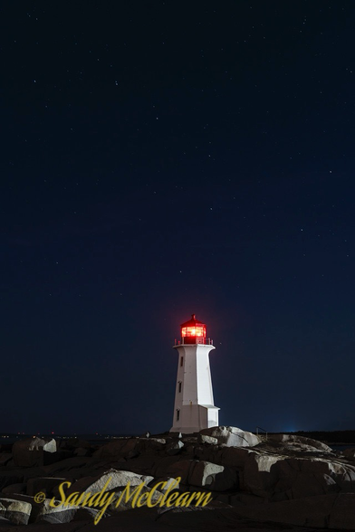 Lighthouse at night showing a red light with the Big Dipper constellation in the sky above.