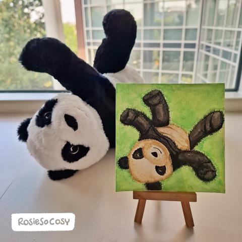 Watercolour painting of a panda on its back in the green grass, arms and legs spread wide. Behind the painting is the actual panda plush in the same position. Panda is smiling and being silly. Actual photo was taken in the Children's Hospital in Utrecht.