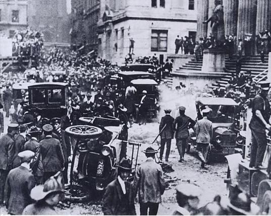 Aftermath of the bombing, with crowds in the street, overturned and damaged cars, police and fire fighters.