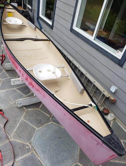A fibreglass canoe with faded paint, showing a smooth inner floor without a visible support beam