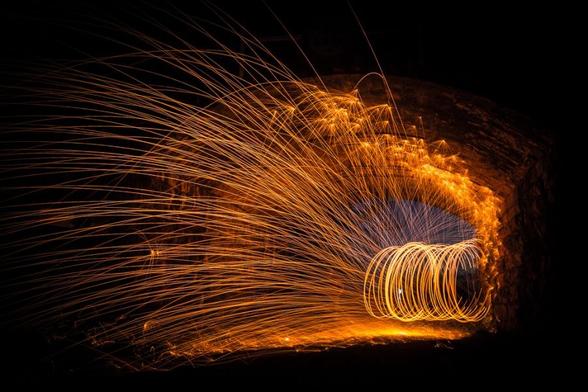 Sparks fly through the air under a bridge in a long exposure photo.