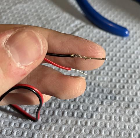 A red and black wire held in my fingers. The end of the red wire is stripped exposing the bare wire, while the end of the black wire has a JST SM DIP male pin crimped onto it