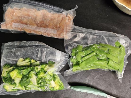 Three vacuum packed packages are shown: one has fully cooked roasted chicken in it, a second has fully cooked broccoli in it with an ice cube, the third has fully cooked snap peas in it also with an ice cube.  The ice cube within the packs allows for some added moisture as they heat up.