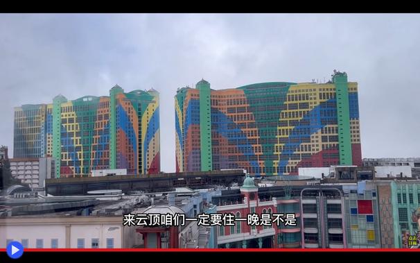 Coppia di edifici multipiano molto simili tra loro, coperti da strisce colorate gialle, verdi, arancioni e blu. Di fronte è visibile la cima delle strutture di un parco a tema.